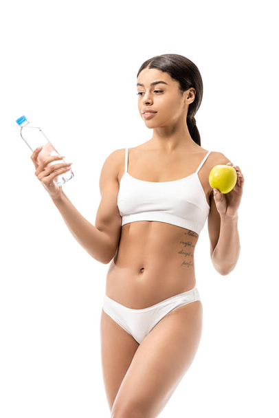mince jeune afro-américaine en sous-vêtements tenant bouteille d'eau et pomme verte isolé sur blanc
 - Photo, image
