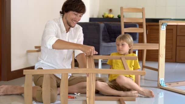 Father and son assemble wooden furniture from small parts. Little boy helps his father to assemble a chair. - Footage, Video