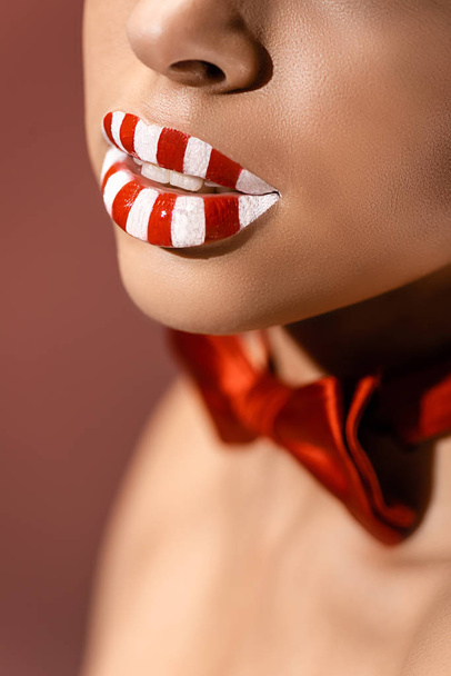 close-up partial view of beautiful red and white striped female lips isolated on burgundy - 写真・画像