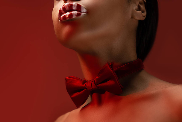赤い蝶ネクタイとブルゴーニュに分離されたストライプの唇を持つ魅惑的な若いアフリカ系アメリカ人女性のクロップ撮影 - 写真・画像