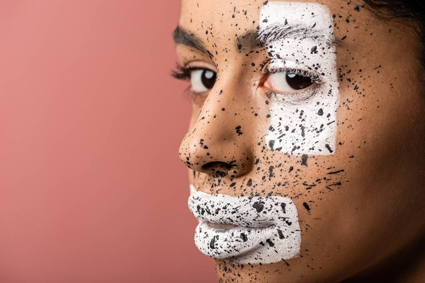 close-up view of beautiful african american woman with white and brown paint on face looking at camera isolated on pink  - Valokuva, kuva