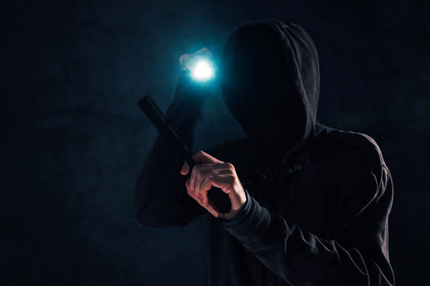 Armed robbery, criminal with hoodie holding gun and torchlight and attacking in dark, low key selective focus - Foto, imagen