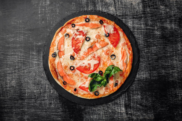 Pizza con queso, trucha, tomates, aceitunas y camarones en una piedra y una pizarra de tiza negra, vista superior
. - Foto, imagen