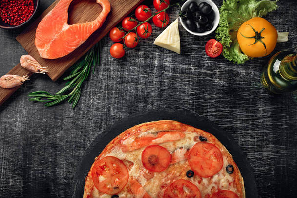Pizza met kaas en forel, tomaten, olijven, garnalen op krijt bord, bovenaanzicht. - Foto, afbeelding