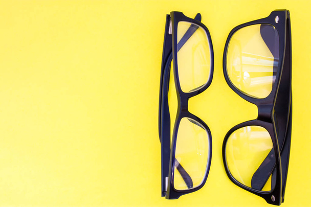 Etiketler, başlıklar için yarım fotoğraf net alanı ile yukarıdan sarı üniforma arka plan görünümü nde iki siyah gözlük. Gözlük seçimi konsept fotoğraf, optometrist iş, reçete dükkanı - Fotoğraf, Görsel