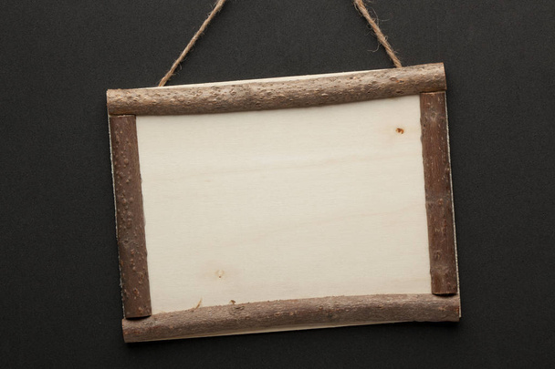 Cartel de madera en blanco colgado de una cuerda sobre fondo negro. Lugar vacío para tu texto
 - Foto, Imagen