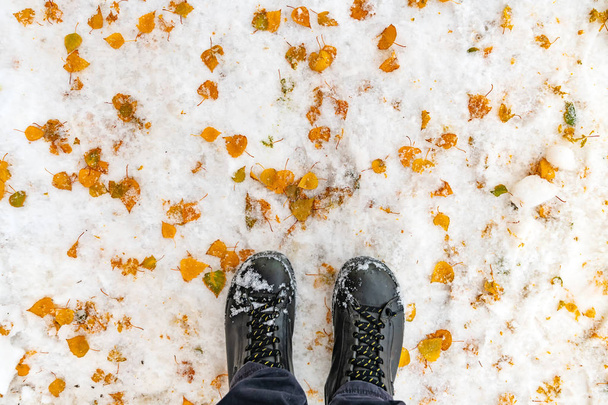 Male feet in boots standing in winter snow covered with yellow leaves - Fotografie, Obrázek