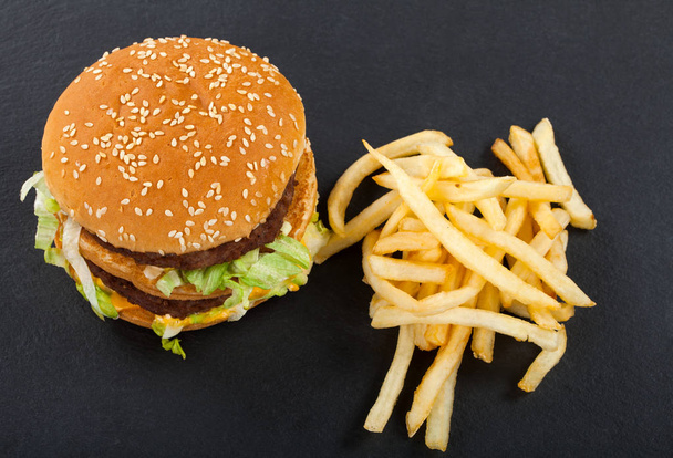 Succulent double cheeseburger with beef, cheddar and lettuce and french fries on black background. Top view - 写真・画像