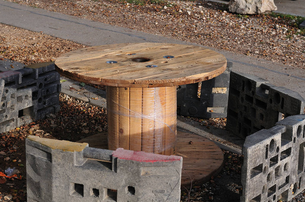 Rastplatz neben Baustelle, improvisiert mit leerer hölzerner Kabelspule und Ofenmöbeln mit provisorischem Zaun - Foto, Bild