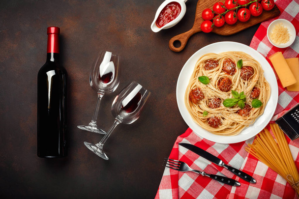 Pâtes spaghetti aux boulettes de viande, sauce tomate cerise, fromage, verre à vin et bouteille sur fond rouillé, vue sur le dessus
. - Photo, image