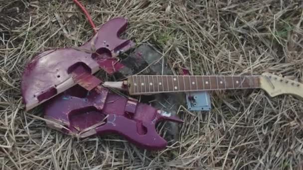 枯れた干し草、トップ ビューで横になっている紫の壊れたギターのクローズ アップ。在庫があります。壊れたエレキギター パーツ紫デッキと枯れた草の背景に茶色の首. - 映像、動画