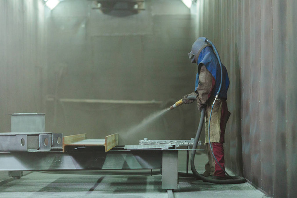 Sandblast. Blasting metal. An employee prepares a metal part for painting. A harsh man works in the factory. - Photo, Image