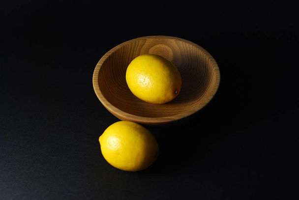 лимонні фрукти на чорному фоні в тарілці з природного матеріалу
 - Фото, зображення