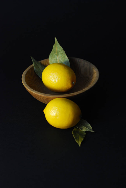 lemon fruits on a black background in a plate of natural material - Фото, изображение