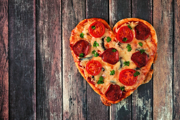 Heart shaped pizza for Valentines Day on a dark wood background. Above view. - Foto, imagen