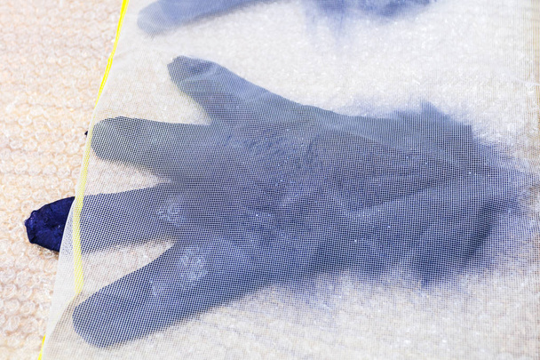 Werkstatt für Handfertigung eines Fleecehandschuhs aus blauer Merino-Schafwolle im Nassfilzverfahren - Nassfilzhandschuh mit neuen Fasern unter Kunststoffnetz - Foto, Bild