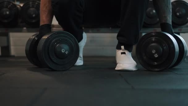 man picks up dumbbells from floor for exercise in gym - Metraje, vídeo