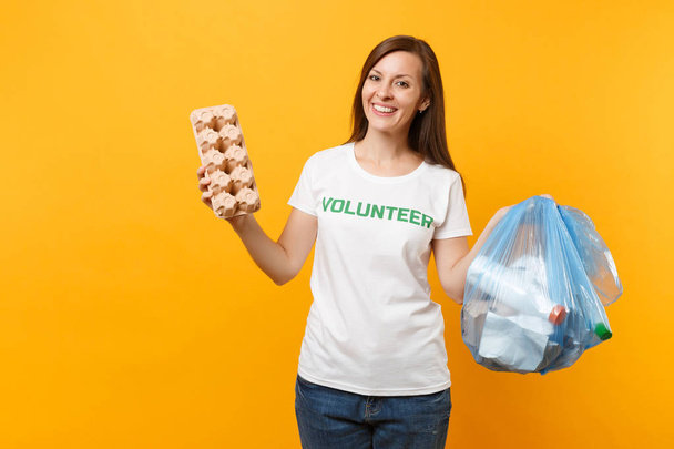 Vapaaehtoinen nainen t-paidassa, keltaisella pohjalla eristetty jätesäkki. Vapaaehtoista apua, armeliaisuutta. Ympäristön saastuminen. Lopeta luonnon roskat ympäristön suojelun käsite
 - Valokuva, kuva