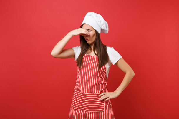 Háziasszony női szakács szakács vagy csíkos kötény, fehér póló, karimátlan kis női kalap szakácsok kalap, piros háttér elszigetelt baker. Házvezetőnő nő közel orr kézzel, mert illata. Mintája fel másol tér fogalma - Fotó, kép