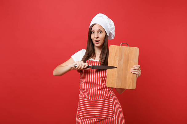 Dona de casa cozinheiro chef feminino ou padeiro em avental listrado, t-shirt branca, chapéu de chefs toque isolado no fundo da parede vermelha. Mulher empregada segurando tábua de corte de madeira, faca. Mock up conceito de espaço de cópia
 - Foto, Imagem