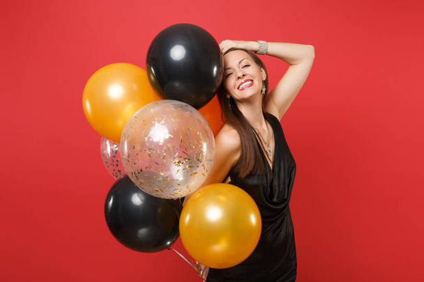Usmívající se dívka v černých šatech oslavili uvedení ruku na hlavu držet s vrtulovým pohonem izolované na červeném pozadí. Sv. Valentýn Mezinárodního dne žen den šťastný nový rok narozeniny maketa holiday party koncept - Fotografie, Obrázek