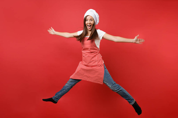 Hospodyňka žena kuchař kuchař nebo baker v pruhované zástěry bílé tričko, toque šéfkuchaři klobouk izolované na pozadí červené zdi. Žena, Hospodyně po celé délce portrét skákat vysoko. Vysmívat se koncepce prostoru kopie - Fotografie, Obrázek