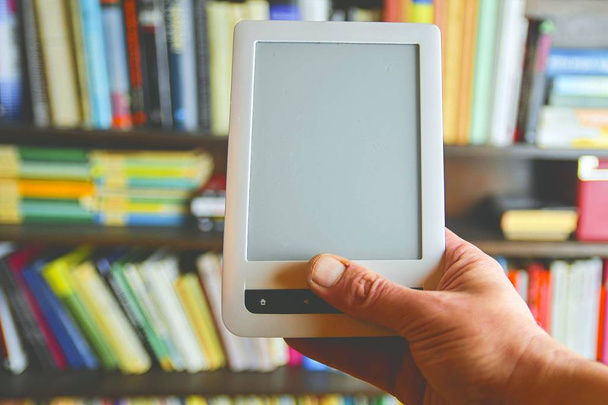 EBook nebo digitální čtení tablet zařízení. E-knihy v mans ruku. Na pozadí je police s jasně skutečné knihy. Online nakupování knih koncept - Fotografie, Obrázek