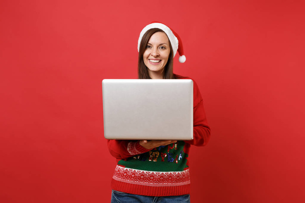 ノート パソコン pc コンピューターで作業を使用してクリスマス帽子セーター サンタ少女を見事な明るい赤の背景に分離されました。幸せな新しい年 2019年お祝いの休日党の概念。コピー スペースをモックアップします。 - 写真・画像