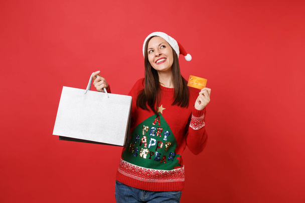 verträumtes Weihnachtsmädchen, das aufblickt, Kreditkartenpakete mit Einkäufen nach dem Einkauf isoliert auf leuchtend rotem Hintergrund hält. Frohes neues Jahr 2019 Feier Feiertag Party-Konzept. Attrappe Kopierraum - Foto, Bild