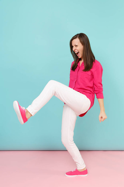 Retrato de larga duración de la diversión enojada joven bonita mujer en camisa rosa blusa, pantalones blancos posando aislado en brillante rosa azul pastel estudio de fondo de la pared. Concepto de estilo de vida. Simular espacio de copia
 - Foto, imagen
