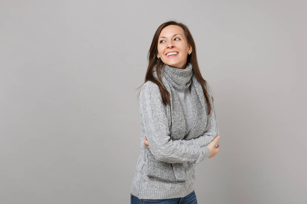 Радостная молодая женщина в сером свитере, шарф, держась за руки, смотрит в сторону на сером фоне. Здоровый образ жизни моды, люди искренние эмоции, концепция холодного сезона. Пространство для копирования
 - Фото, изображение
