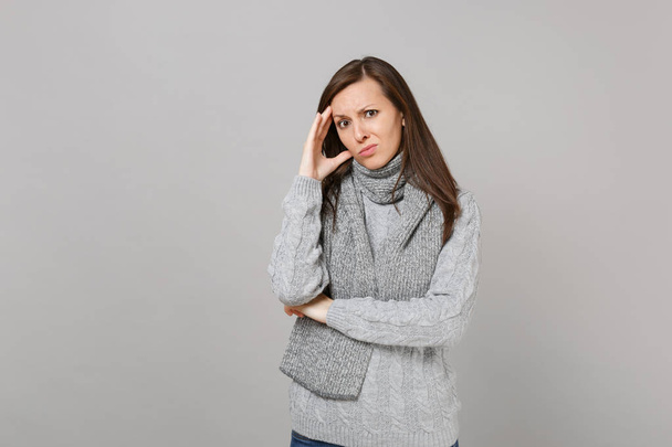 Concerned pensive young woman in gray sweater, scarf putting hand on head isolated on grey wall background in studio. Healthy fashion lifestyle people emotions cold season concept. Mock up copy space - Foto, Imagen
