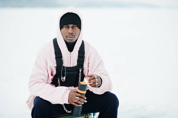 African american fisherman with thermos sitting on frozen lake. Winter fishing. - Foto, Imagem