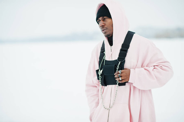 Stylish urban style african american man in pink hoodie posed at frozen lake in winter. - 写真・画像