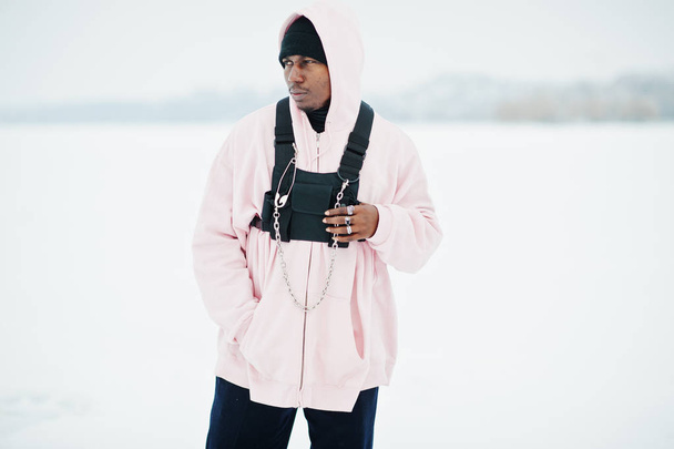 Stylish urban style african american man in pink hoodie posed at frozen lake in winter. - Zdjęcie, obraz