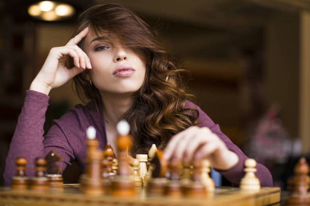 Woman playing chess indoor and thinking position, find winning move, strategy - Фото, изображение
