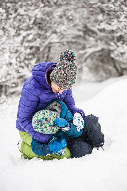A gyerek anyja ölelést. A fiú anyja egy téli séta. A gyermek egy térdzokni szórakozni az anyjával. A nő játszik a fiával a hóban. A család időt tölt együtt. Családi értékek. - Fotó, kép