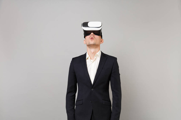 Portrait of young business man in classic black suit and white shirt looking up in headset isolated on grey wall background in studio. Achievement career wealth business concept. Mock up copy space - Φωτογραφία, εικόνα