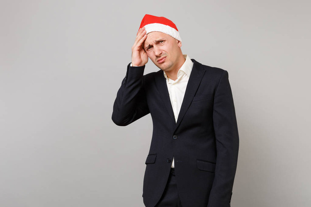 灰色の背景に分離された頭痛を持っている頭に手を置いてクリスマス帽子の男を不満のビジネス。達成のキャリア豊富なビジネス。幸せな新しい年 2019年お祝い休日党概念 - 写真・画像