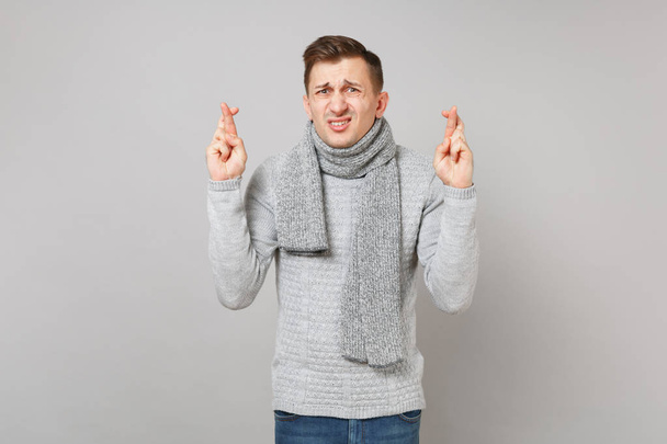 グレーのセーターに戸惑い混乱している若い男が、指が交差維持スカーフ灰色の背景上に分離。健全なライフ スタイル、人々 の心から感情、寒い季節の概念。コピー スペースをモックアップします。 - 写真・画像