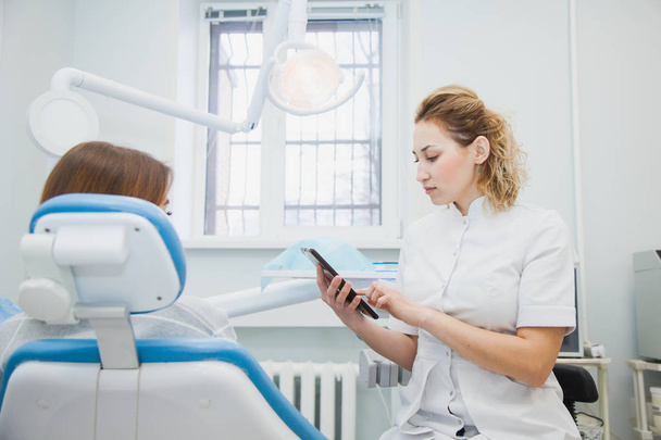 Zahnärztin und Patient diskutieren Behandlungen in einer Tablettenanwendung. Stomatologin zeigt Patientin ihren Fall auf digitaler Applikation - Foto, Bild