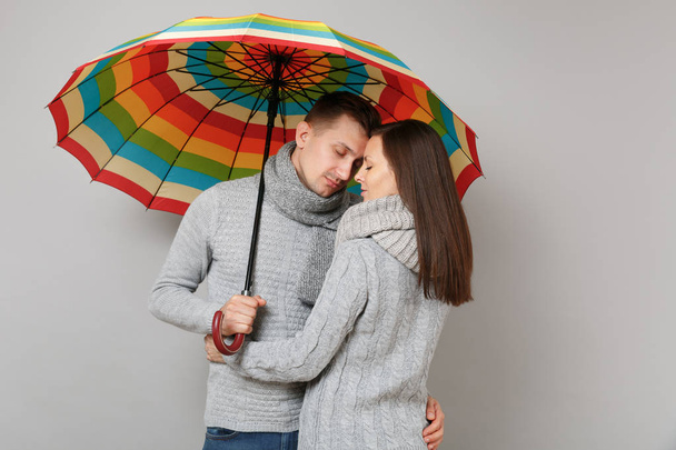 Couple girl guy in gray sweaters scarves together under umbrella isolated on grey wall background, studio portrait. Healthy lifestyle sick disease treatment cold season concept. Mock up copy space - 写真・画像