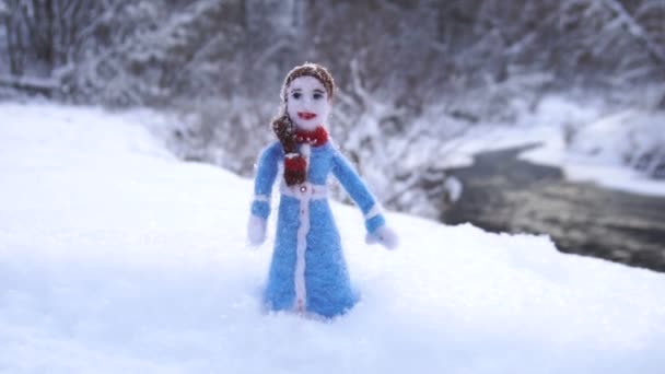 Giocattolo ragazza fatta di lana in piedi in cumulo di neve sullo sfondo fiume invernale
 - Filmati, video