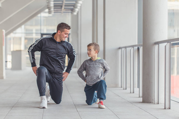 少年と彼の父親は、スポーツ センターで一緒に足のストレッチ体操を行います。父と息子と一緒に時間を費やすし、健康的なライフ スタイルをリードします。一緒にワークアウト。フィットネスの日。スポーティな家族概念.  - 写真・画像