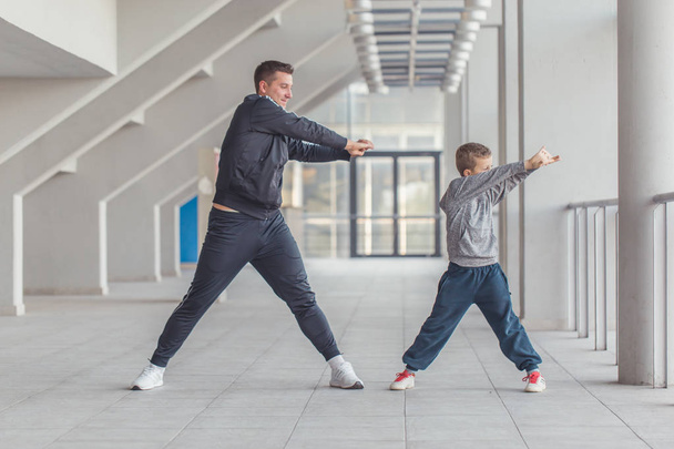 Маленький хлопчик і його батько розтягують руки в спортивному центрі. Батько і син проводять час разом і ведуть здоровий спосіб життя. День фітнесу. Спортивна сімейна концепція
.  - Фото, зображення