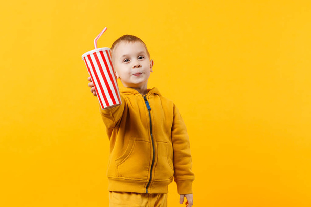 Маленький веселый веселый мальчик 3-4 лет в желтой одежде держать чашку соды изолированы на фоне оранжевой стены, детский студийный портрет. Люди, концепция детского образа жизни. Пространство для копирования
 - Фото, изображение