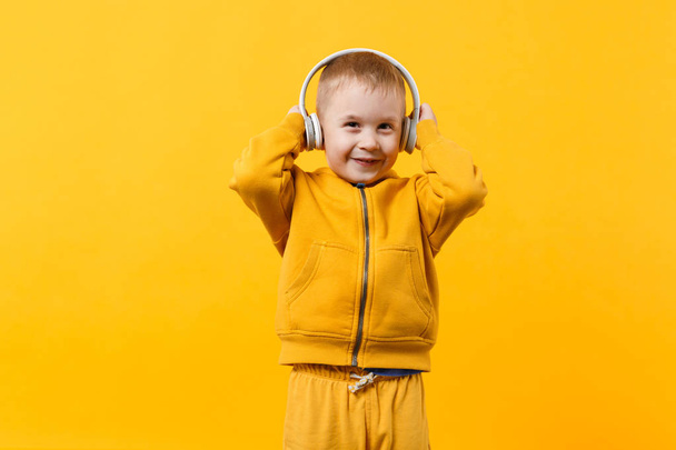 Little kid boy 3-4 years old wearing yellow clothes in headphones isolated on orange wall background, children studio portrait. People sincere emotions childhood lifestyle concept. Mock up copy space - Photo, Image