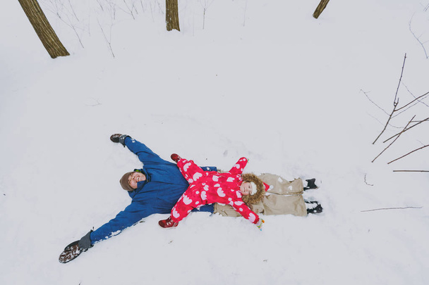 Rodina vtipálek, malá holčička v barevné teplé oblečení šíření ruce, takže sníh andělé při ležící v parku či lesa venku. Zimní zábava, volný čas na dovolené. Milostný vztah životního stylu koncept - Fotografie, Obrázek