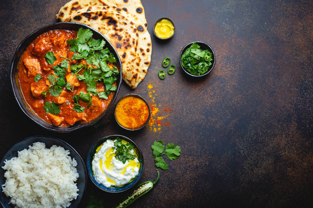 Traditional Indian dish Chicken tikka masala with space for text. Spicy curry meat in bowl, basmati rice, bread naan, yoghurt raita sauce on rustic dark background, top view, close up, copy space  - Photo, Image