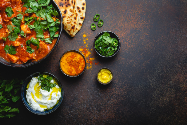 Authentic Indian dish Chicken tikka masala with space for text. Spicy curry meat in bowl with fresh bread naan, yoghurt raita sauce on rustic dark background, top view, close up, copy space  - Photo, Image